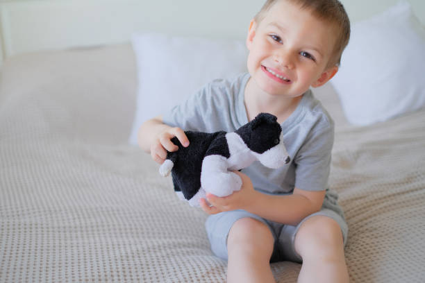 gros plan d’un petit garçon caucasien heureux dans un t-shirt gris allongé sur le lit avec un chien jouet - dog baby t shirt child photos et images de collection