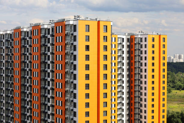 New residential buildings with orange and yellow cladding on background of green park and sky with white clouds stock photo