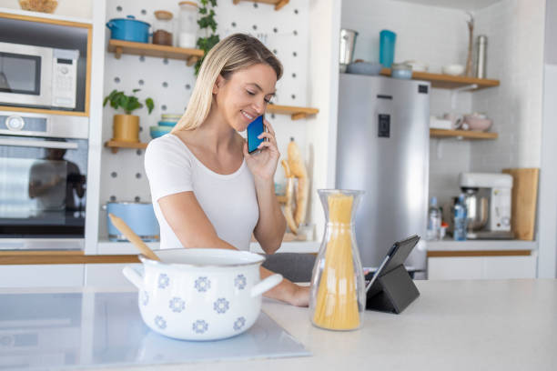 istock Woman on phone call reading recipe from digital tablet when making lunch 1412609186