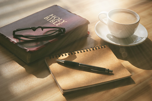 Pray and study the Bible in the morning in the warm sunshine on a bright day. with a cup of coffee and a notebook Placed on a wooden table under the bright morning sun.