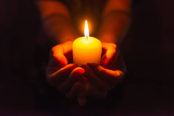 istock Candle in female hands on black dark background.Prayers candle in hands. 1412612189