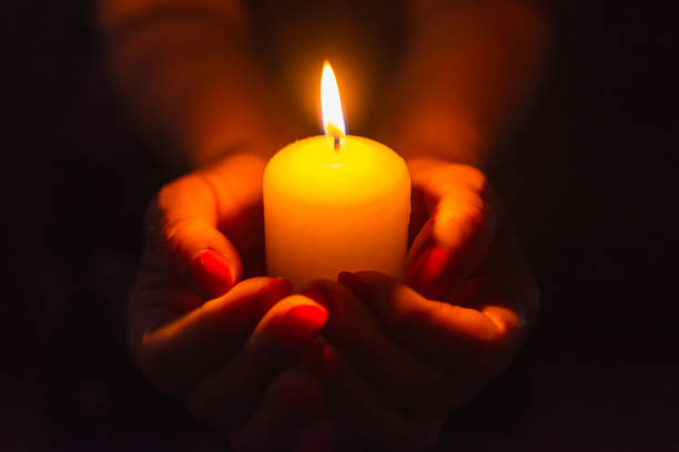 istock Candle in female hands on black dark background.Prayers candle in hands. 1412612191
