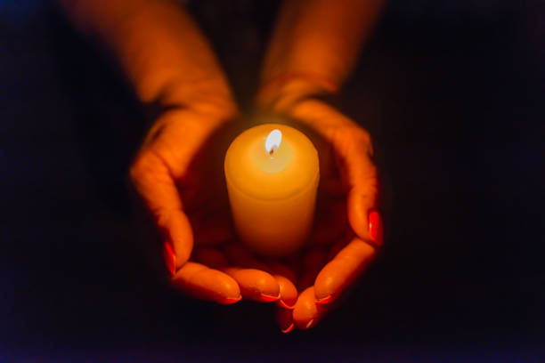 istock Candle in female hands on black dark background.Prayers candle in hands. 1412612202