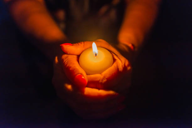 istock Candle in female hands on black dark background.Prayers candle in hands. 1412612205