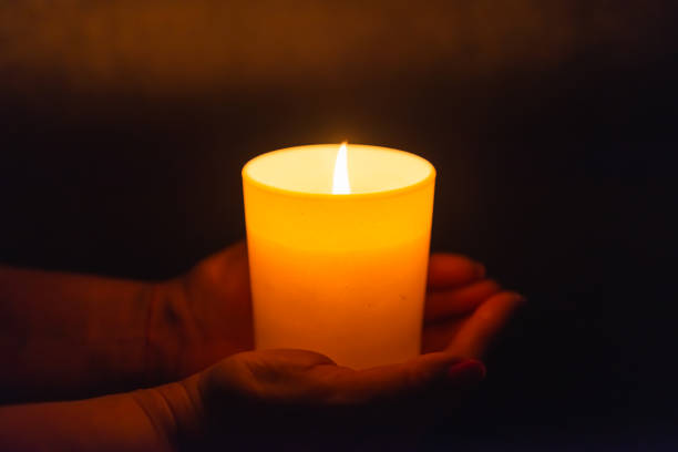 istock Candle in female hands on black dark background.Prayers candle in hands. 1412612217