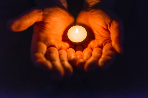 istock Burning candle in a mans hand religion concept.Candle in hands on a dark background. 1412612224