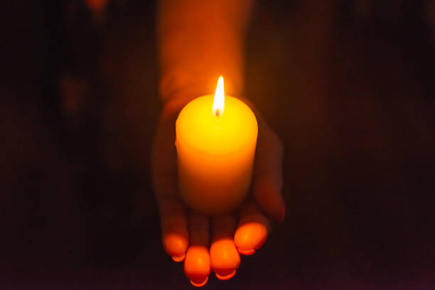 istock Candle in female hands on black dark background.Prayers candle in hands. 1412612249
