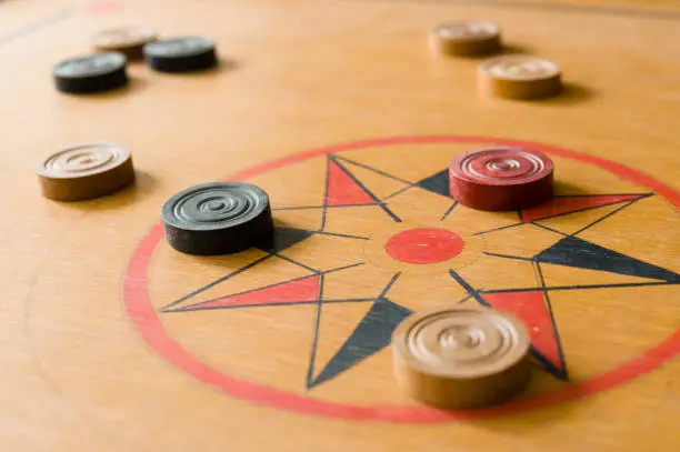 Photo of A game of carrom with scattered stones on the board around the center star