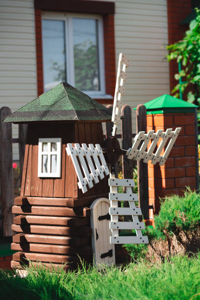 istock A small decorative wooden dark windmill with while blades and a small white window. Placed against a modern house. Grass and a bush on the foreground 1412619351