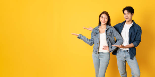 istock Two Young good looking asian couple using isolated on yellow background presenting to copy space 1412621946