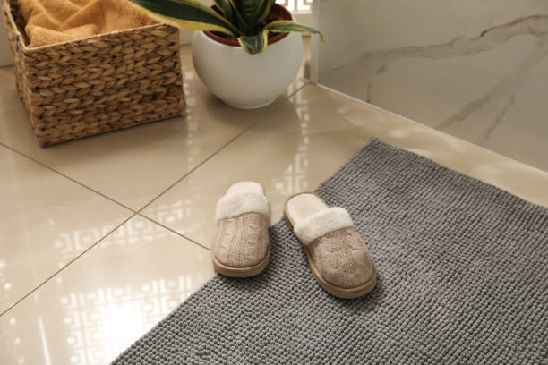 istock Soft grey bath mat and slippers on floor indoors 1412622677