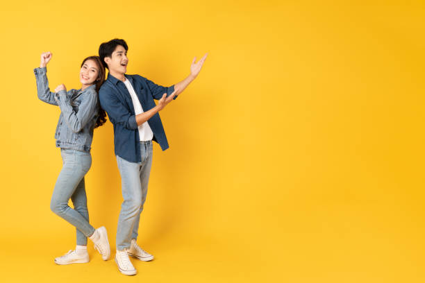 istock Two Young good looking asian couple using isolated on yellow background presenting to copy space 1412622682