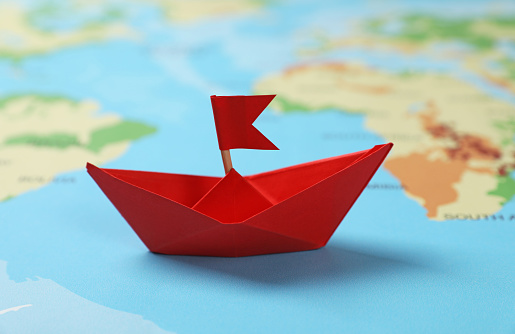 Red paper boat with flag on world map