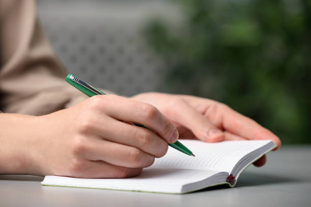 istock Woman writing with pen in notebook at table indoors, closeup. Space for text 1412623495