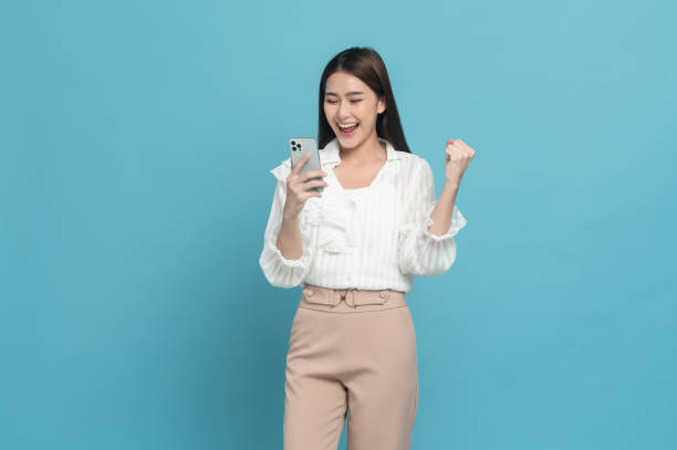 Young beautiful asian woman with smart casual cloth use smartphone isolated on blue background stock photo