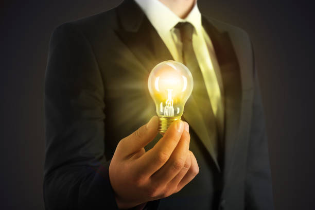 istock Glow up your ideas. Businessman holding light bulb on dark background, closeup 1412624710