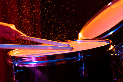 Dynamic scene. man playing the snare drum on a colored background, the concept of musical instruments with splashing water on dark background with orange and blue studio lighting