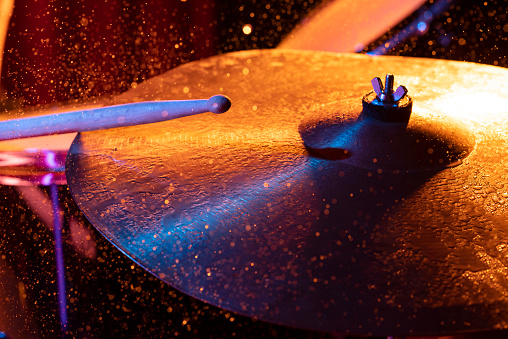 Dynamic scene. man playing the  drum plate on a colored background, the concept of musical instruments with splashing water on dark background with orange and blue studio lighting