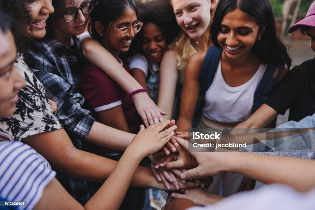 Group of multicultural teenagers putting their hands together in unity Group of multicultural teenagers smiling cheerfully while putting their hands together in a huddle. Happy young students stacking their hands in unity. Multiracial Group Stock Photo