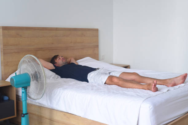 Young man laying and sleeping against fan on a hot summer day stock photo