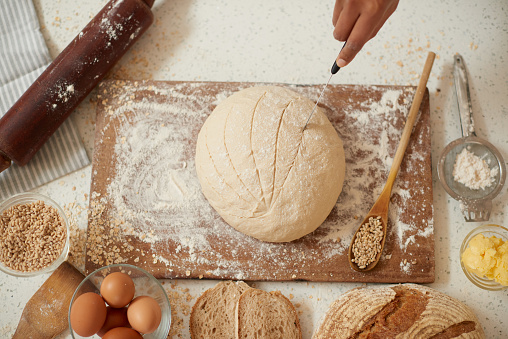 baker's hands holding knife giving shape to dough. sprinkled with flour close-up along with some eatable items. yeast dough ready for pizza, burn or bread. Leavened yeast dough ready for use for baking bread, pizza, pies.