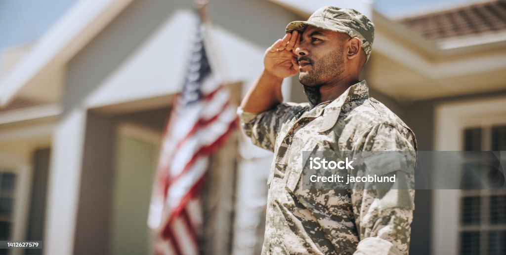 Patriotic young soldier saluting outdoors Patriotic young soldier saluting while standing outside his home. Member of the United States Marine Corps showing honour and respect on Veterans Day. US Veteran's Day Stock Photo