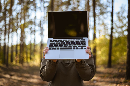 Woman holding laptop with blank screen in woodland