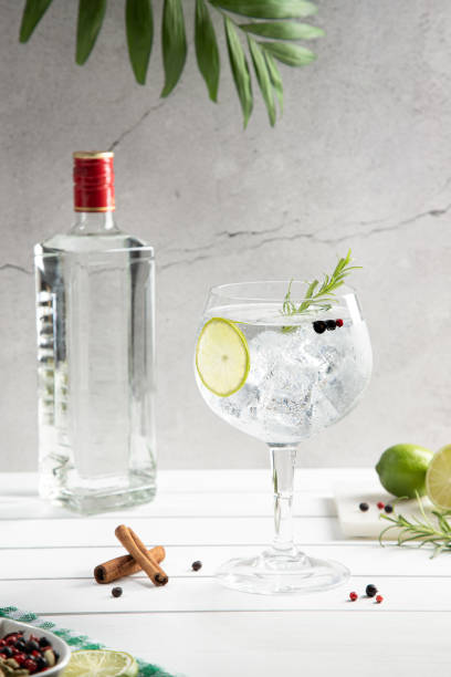 istock Cold glass of gin tonic and bottle on white wooden base on light background. Vertical format. 1412629152