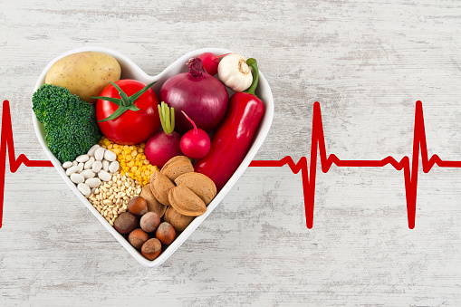 Heart health concept with related foods in white heart shaped bowl. potato red peppers, broccoli, radish, red onion, garlic, dry beans, almonds, nuts, and other legumes were arranged in heart shape plate