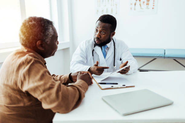 istock Serious doctor is talking to male patient while holding a tablet computer. 1412635055