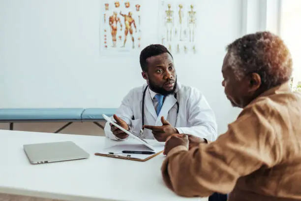 Photo of Friendly and Cheerful Family Doctor is Reading Medical History of Senior Male Patient During Consultation