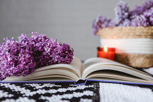 Wicker basket with lilacs, a candle, an open book on the table.Good morning concept.