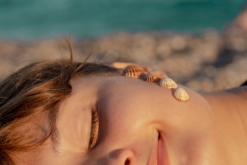 Woman posing with seashells on her face.\n\nWoman with seashells on her face daydreaming on the beach.