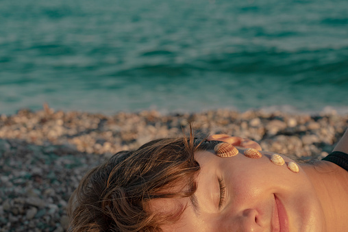 Woman posing with seashells on her face.

A woman sunbathing on the beach with seashells on her face.