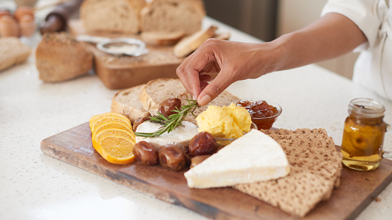 Closeup of unknown chef arranging savory board on kitchen counter in restaurant. Zoomed in on woman cook placing orange slices with olives, cheese, crackers, bread, butter and strawberry jam for tapas