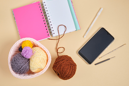 smartphone, notebook and knitting hooks and threads in a basket on a beige background, online knitting training, blogging on needlework top view