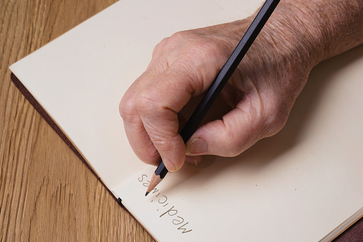 Detail of an elderly woman's hands holding a pencil and writing the word 