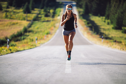 Mid adult woman jogging over empty road on mountain. She is fit and muscular, professional sky runner