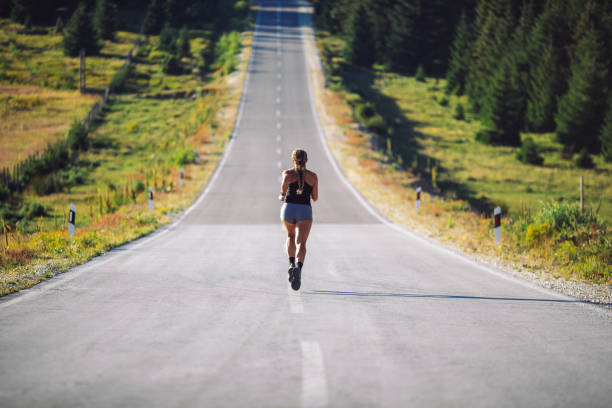 Mid adult woman jogging over empty road on mountain. She is fit and muscular, professional sky runner