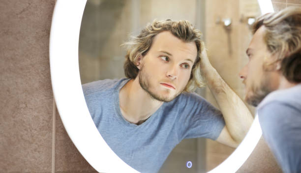 istock young man looking in the mirror,combing his hair,looking at problems on face 1412644973