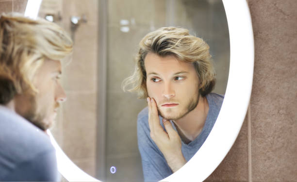 istock young man looking in the mirror,combing his hair,looking at problems on face 1412644976