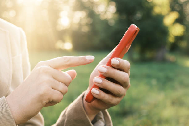 Closeup of female hands using a smart phone, nature background. Woman using mobile phone in sunset outdoors. Unrecognizable person touching smartphone screen. Unknown girl holding cellphone outside. Roaming. Mobile phone signal. Wireless service providers. primer plano de manos femeninas usando un teléfono inteligente, fondo de la naturaleza. mujer usando el teléfono móvil al atardecer al aire libre. persona irreconocible tocando la pantalla del teléfono inteligente. chica desconocida sosteniendo el tel�