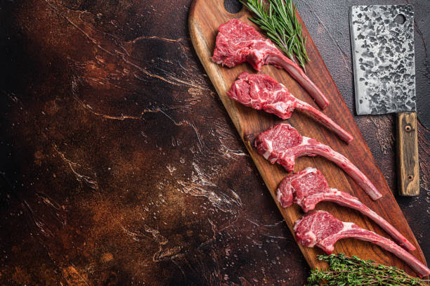 istock Raw Lamb chop steak on butcher board with rosemary and thyme. Dark background. Top view. Copy space 1412652224