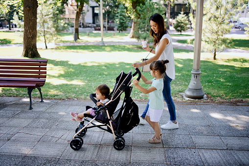 Young mother and her little daughters walking in public park