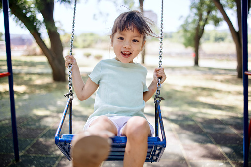 A young girl playing on a push swing at a public park in Hexham, North East England during Autumn. She has her arms outstretched while looking at the camera and smiling.