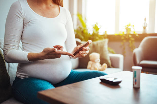 Happy Pregnant woman with glucometer checking blood sugar level at home. stock photo