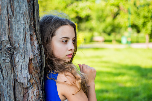 Girl long curly hair lean on tree trunk, lonely child.