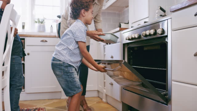 Parent teaching excited son to cook or bake at home, having fun bonding and learning. Happy, carefree child learning cooking skills with his mother. Family spending free time together in the morning