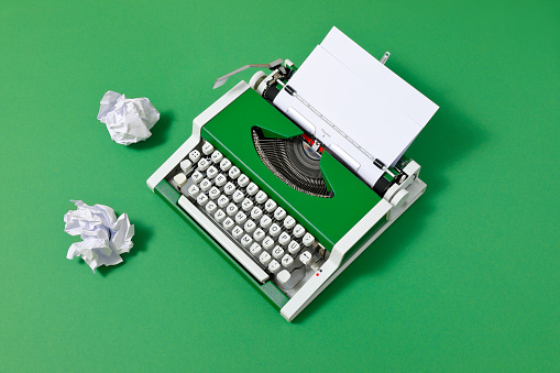 Green 70s typewriter with crumpled paper and a blank page on green backround