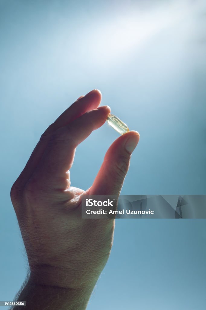 Fish oil pill in man's hand facing light and light blue background. Medical minimal creative concept. Nutritional supplements, vitamins, vitamin D, omega 3. Acid Stock Photo